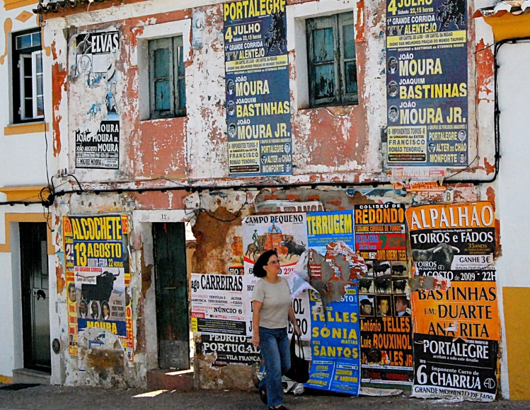 Una mujer pasa por una calle de Monforte, junto a una fachada plagada de carteles de rejoneo